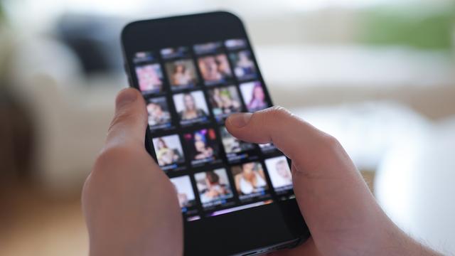 Zwei Hände halten ein Handy. Auf dem Bildschirm sieht man leicht verschwommen mehrere Fotos von Frauen. 