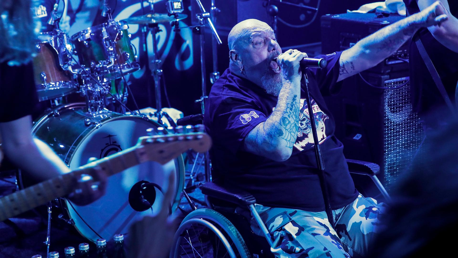 Paul Di'Anno sitzt im Rollstuhl auf der Bühne und performt.