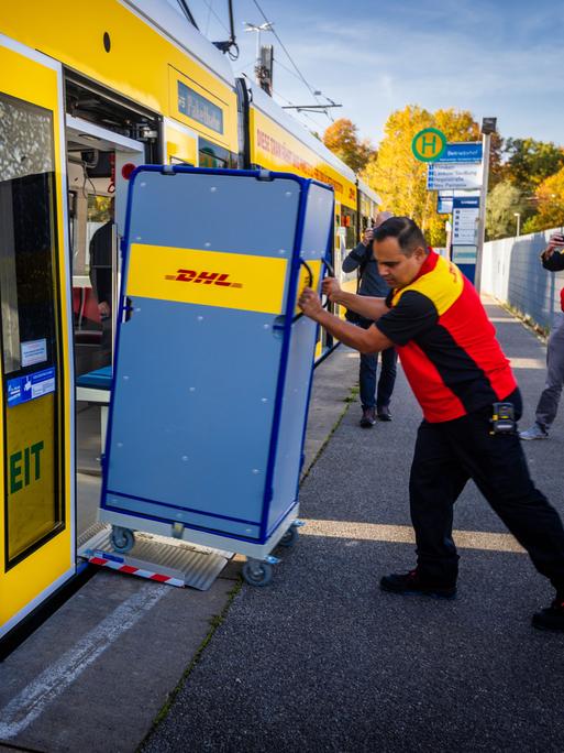 Ein Mitarbeiter der Deutschen Post schiebt einen Transportwagen für Pakete in eine Straßenbahn.