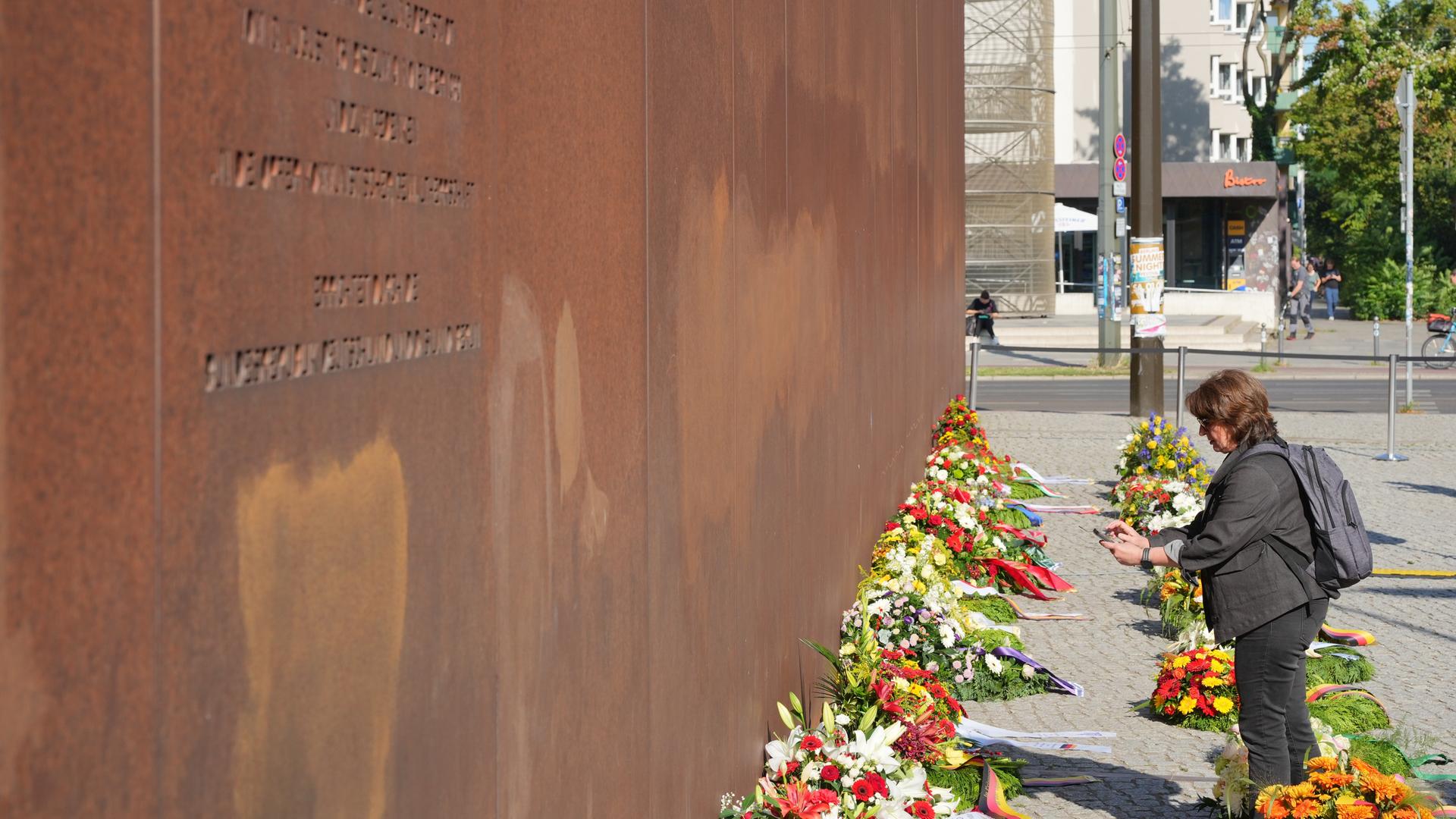 Eine Frau steht vor Beginn der Gedenkfeier zum 65. Jahrestag des Mauerbaus vor den Kränzen an der Gedenkstätte Bernauer Straße. 