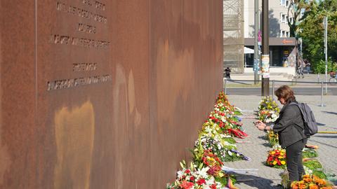 Eine Frau steht vor Beginn der Gedenkfeier zum 65. Jahrestag des Mauerbaus vor den Kränzen an der Gedenkstätte Bernauer Straße. 