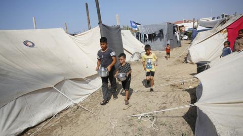 Kinder laufen mit Kochtöpfen zwischen Zelten in einem improvisierten Flüchtlingslager in Khan Yunis im Gazastreifen umher