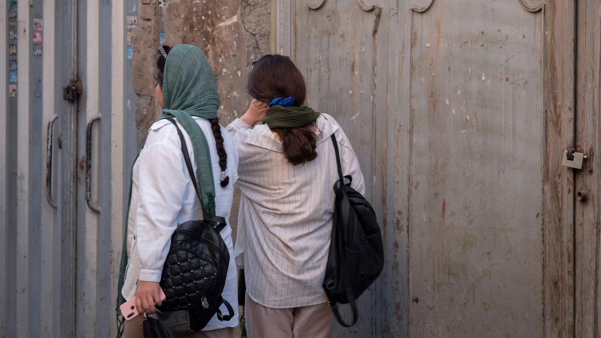 Rückansicht zweier Frauen auf einer Straße in Teheran: Die eine trägt das Kopftuch locker, die andere nur als Halstuch.