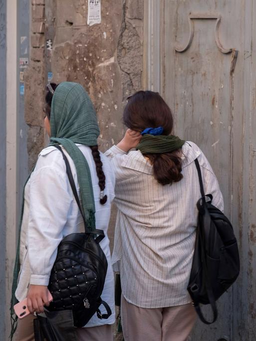 Rückansicht zweier Frauen auf einer Straße in Teheran: Die eine trägt das Kopftuch locker, die andere nur als Halstuch.