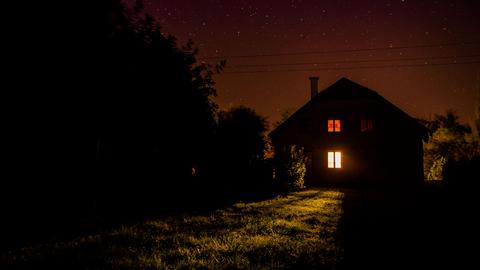 Nachts: Blick auf ein einsames Haus auf einer Wiese, am Rand Bäume.