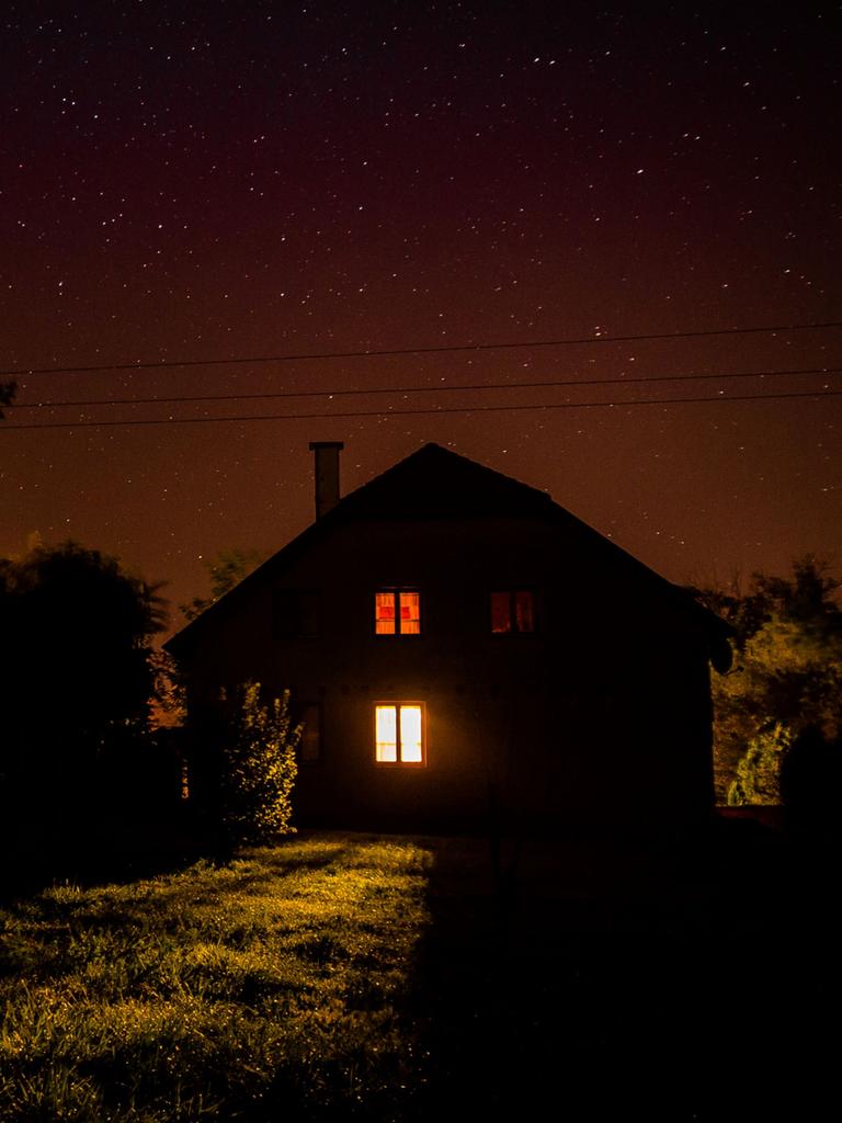 Nachts: Blick auf ein einsames Haus auf einer Wiese, am Rand Bäume.