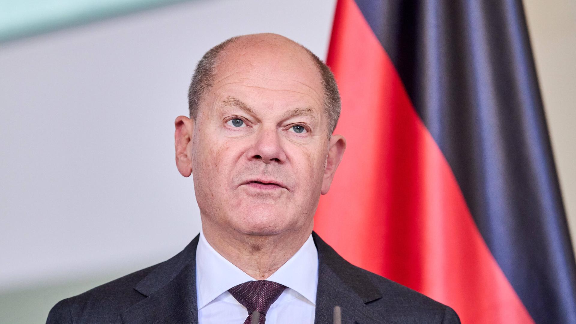 Bundeskanzler Olaf Scholz vor einer Deutschlandfahne.