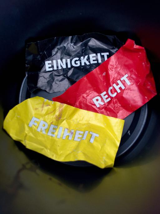 Die Worte "Einigkeit, Recht und Freiheit" auf Flyern in den deutschen Nationalfarben liegen in einem Papierkorb.