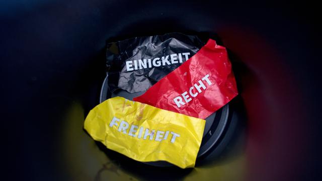 Die Worte "Einigkeit, Recht und Freiheit" auf Flyern in den deutschen Nationalfarben liegen in einem Papierkorb.