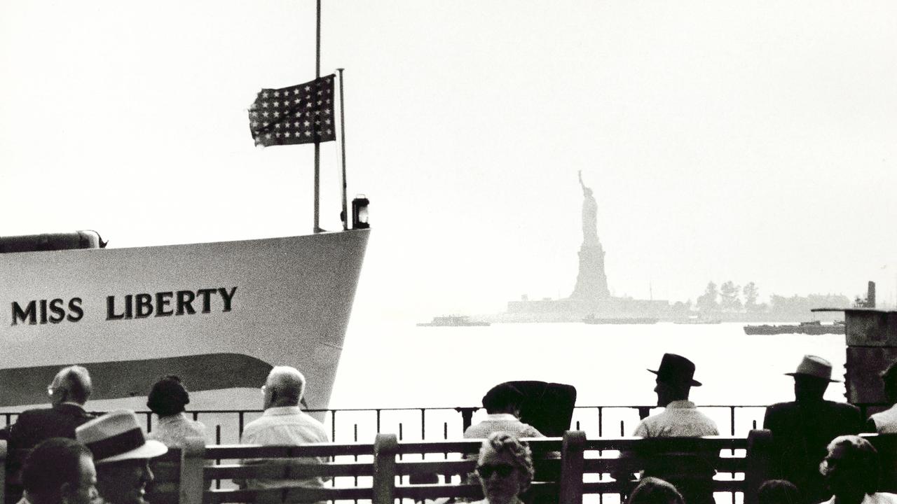 Menschen sitzen in New York am Ufer mit Blick auf die Freiheitsstatue.