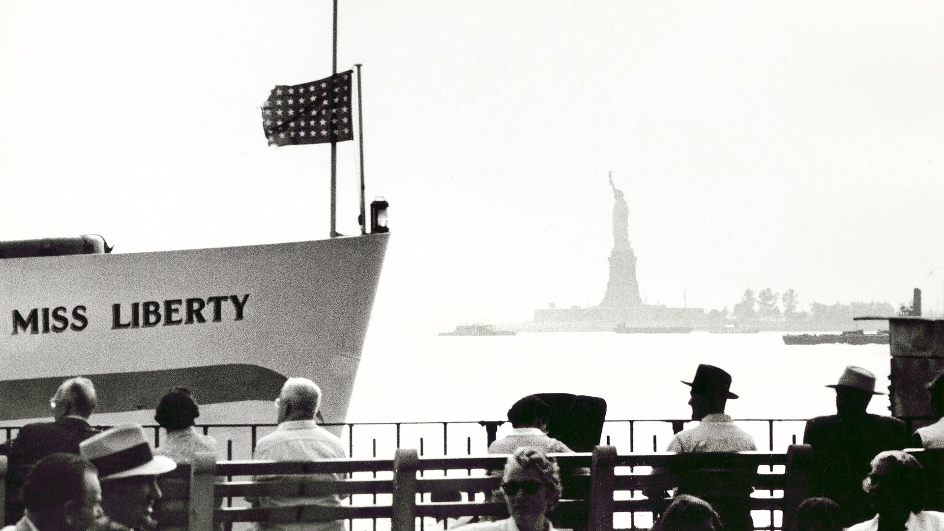 Menschen sitzen in New York am Ufer mit Blick auf die Freiheitsstatue.