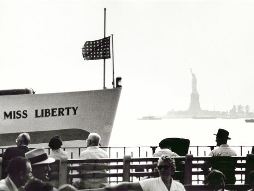 Menschen sitzen in New York am Ufer mit Blick auf die Freiheitsstatue.