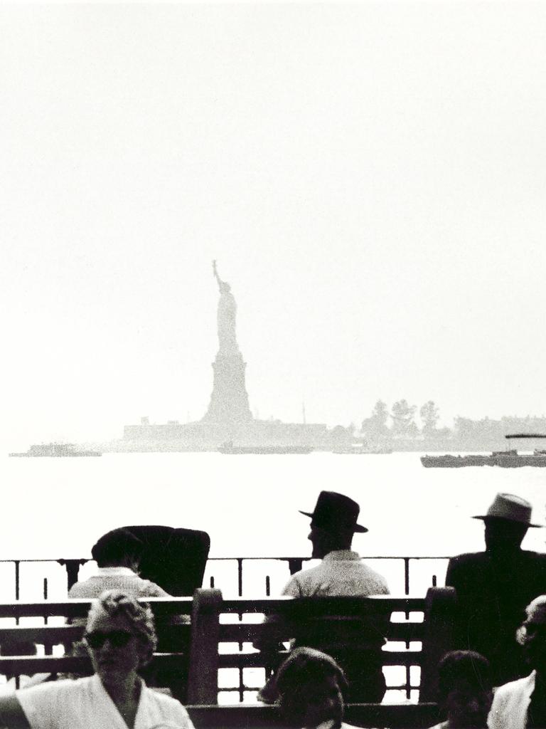 Menschen sitzen in New York am Ufer mit Blick auf die Freiheitsstatue.