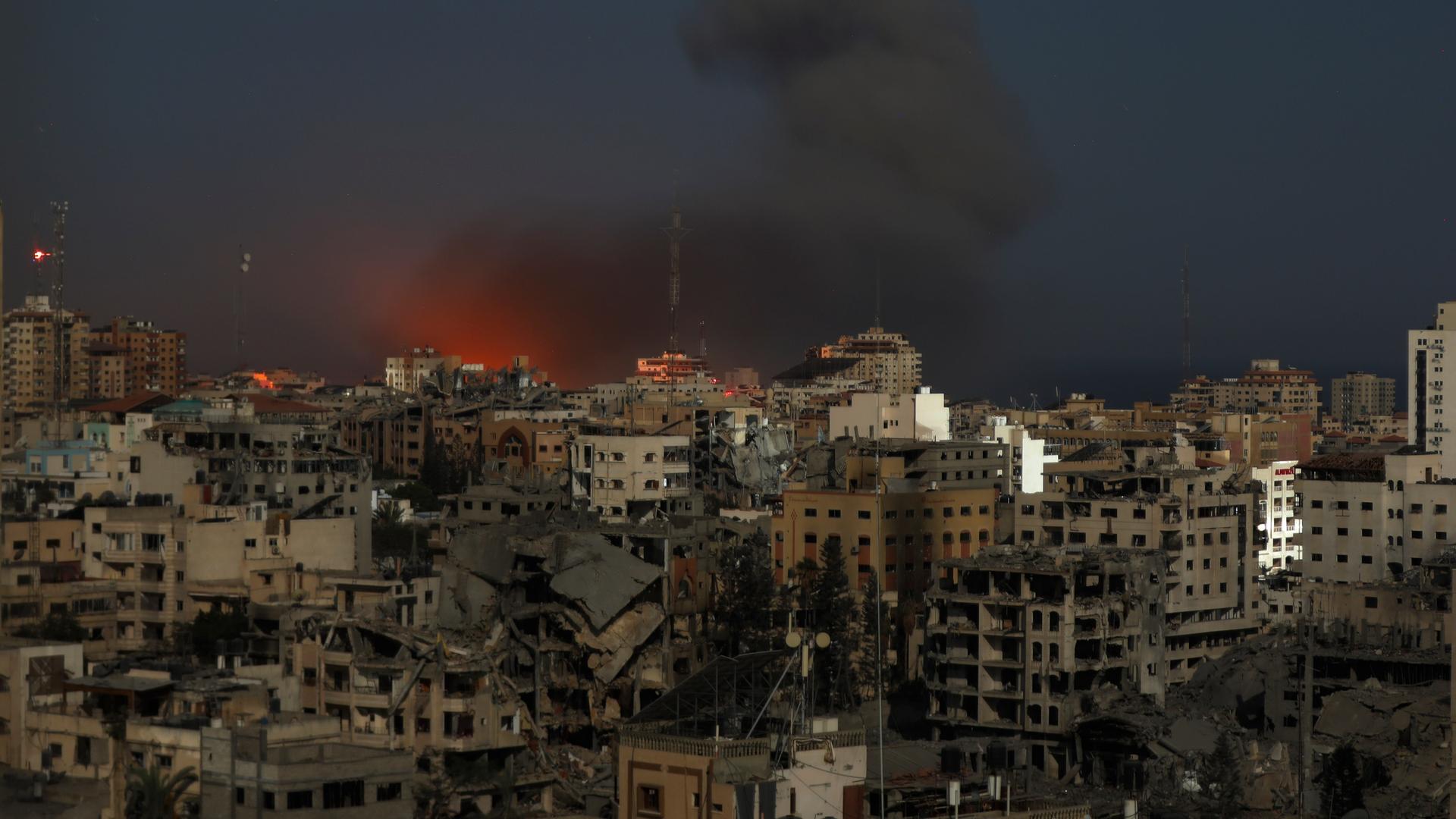 Über zerstörten Hochhäusern von Gaza-Stadt sind Feuer und Rauchwolken am Nachthimmel zu erkennen.