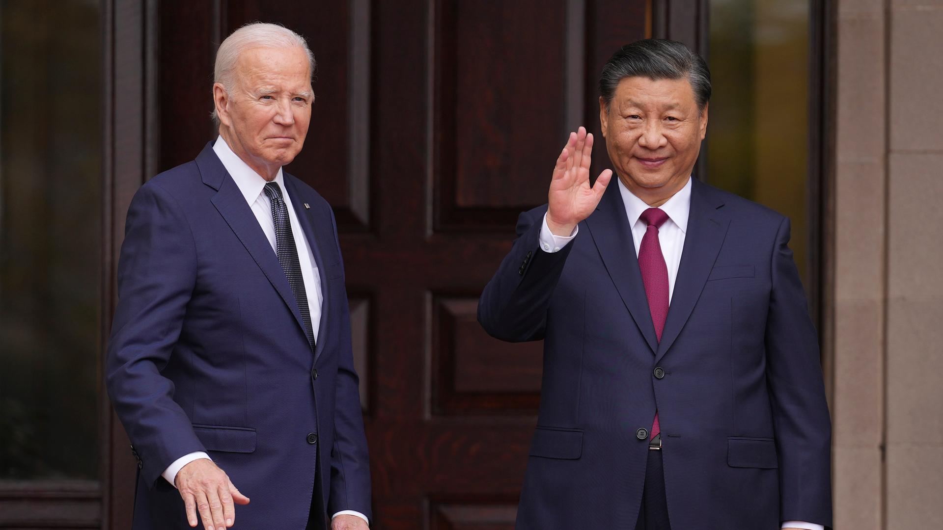 US-Präsident Biden und Chinas Staatschef Xi stehen vor einer dunklen Holztür und winken. Sie tragen beide dunkle Anzüge und Krawatten.