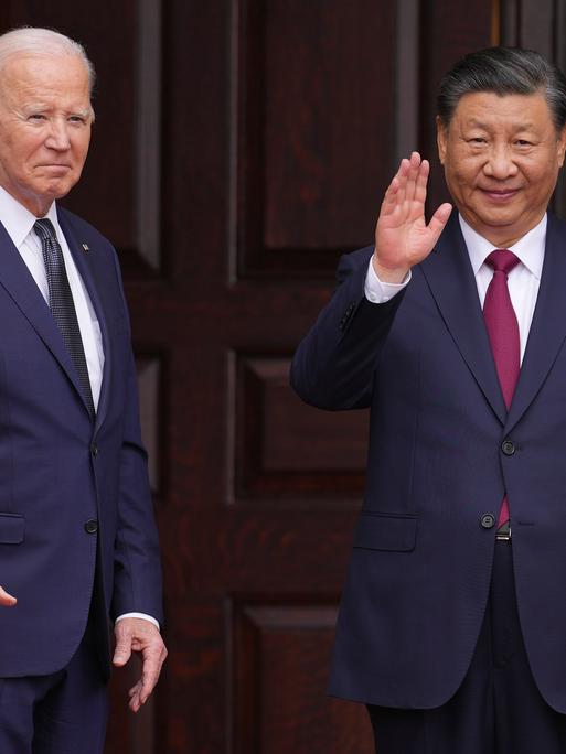 US-Präsident Biden (links) und Chinas Staatschef Xi (rechts) stehen vor einer dunklen Holz-Tür und winken. 