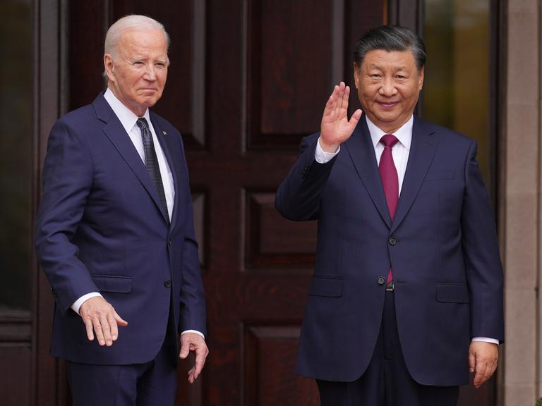 US-Präsident Biden (links) und Chinas Staatschef Xi (rechts) stehen vor einer dunklen Holz-Tür und winken. 