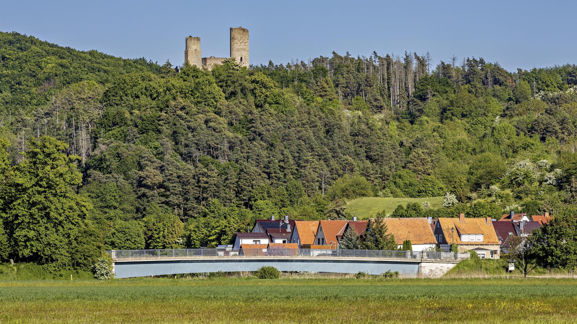 Blick auf eine Burgruine über einem Dorf mit Brücke, umgeben von grünen Wäldern und Wiesen unter klarem Himmel. Die Ruine Brandenburg im Werratal bei Lauchröden in Thüringen (Symbolbild) 