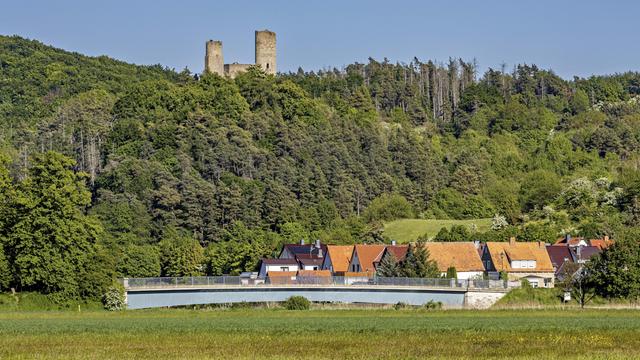Blick auf eine Burgruine über einem Dorf mit Brücke, umgeben von grünen Wäldern und Wiesen unter klarem Himmel. Die Ruine Brandenburg im Werratal bei Lauchröden in Thüringen (Symbolbild) 