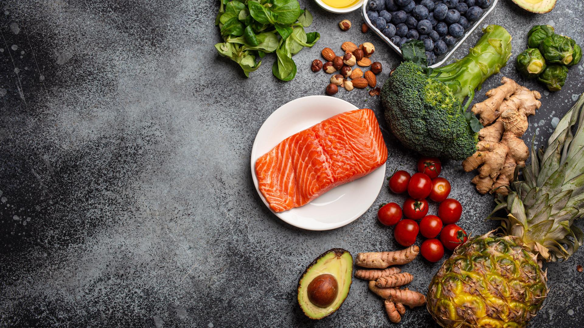 Lachs, Gemüse, Obst, Nüsse und Öle liegen auf einer Platte 