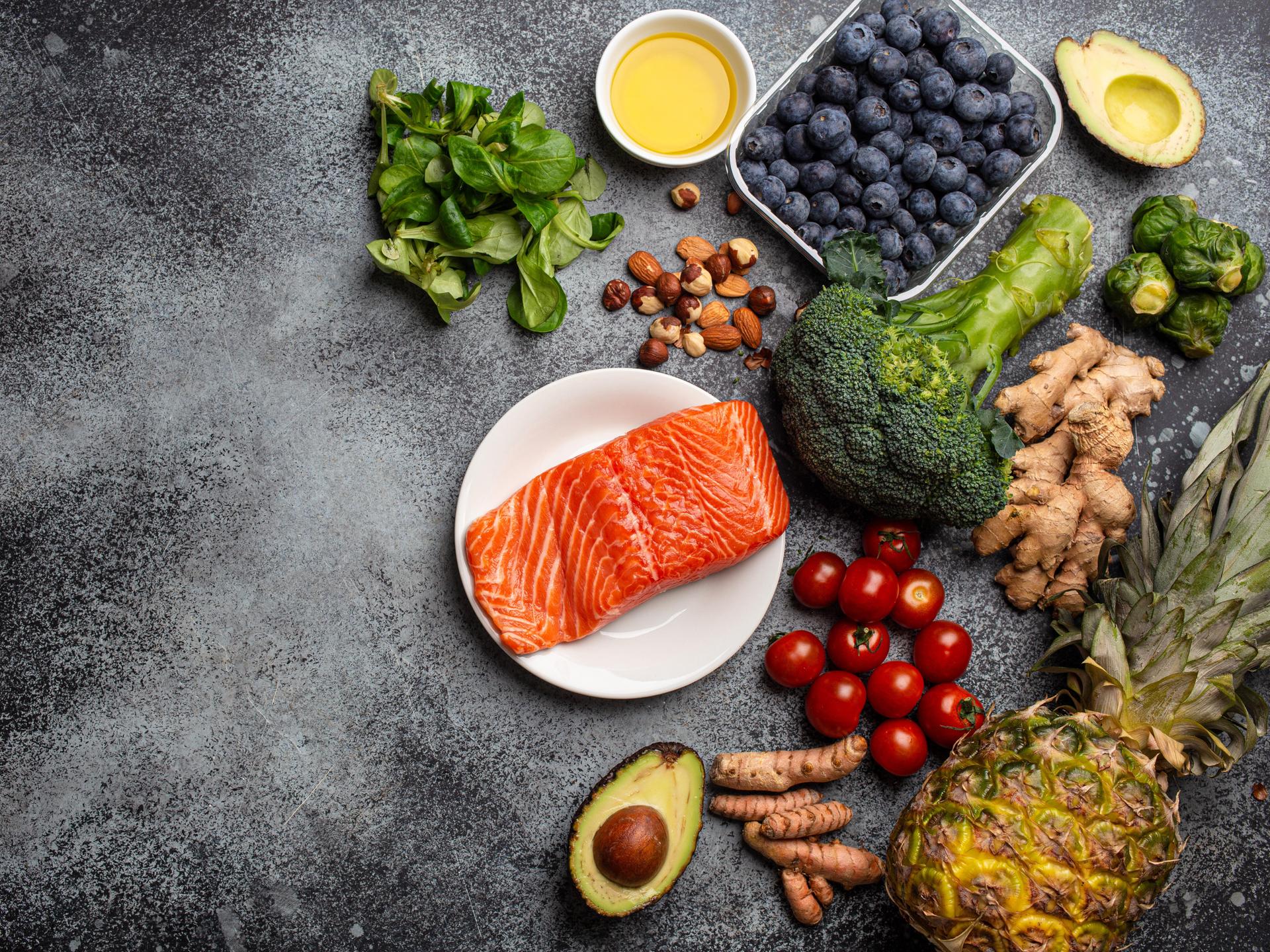 Lachs, Gemüse, Obst, Nüsse und Öle liegen auf einer Platte 