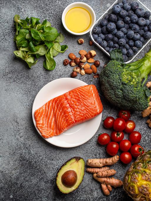 Lachs, Gemüse, Obst, Nüsse und Öle liegen auf einer Platte 