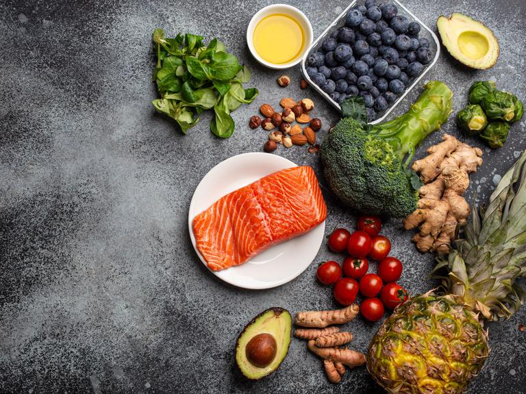 Lachs, Gemüse, Obst, Nüsse und Öle liegen auf einer Platte 