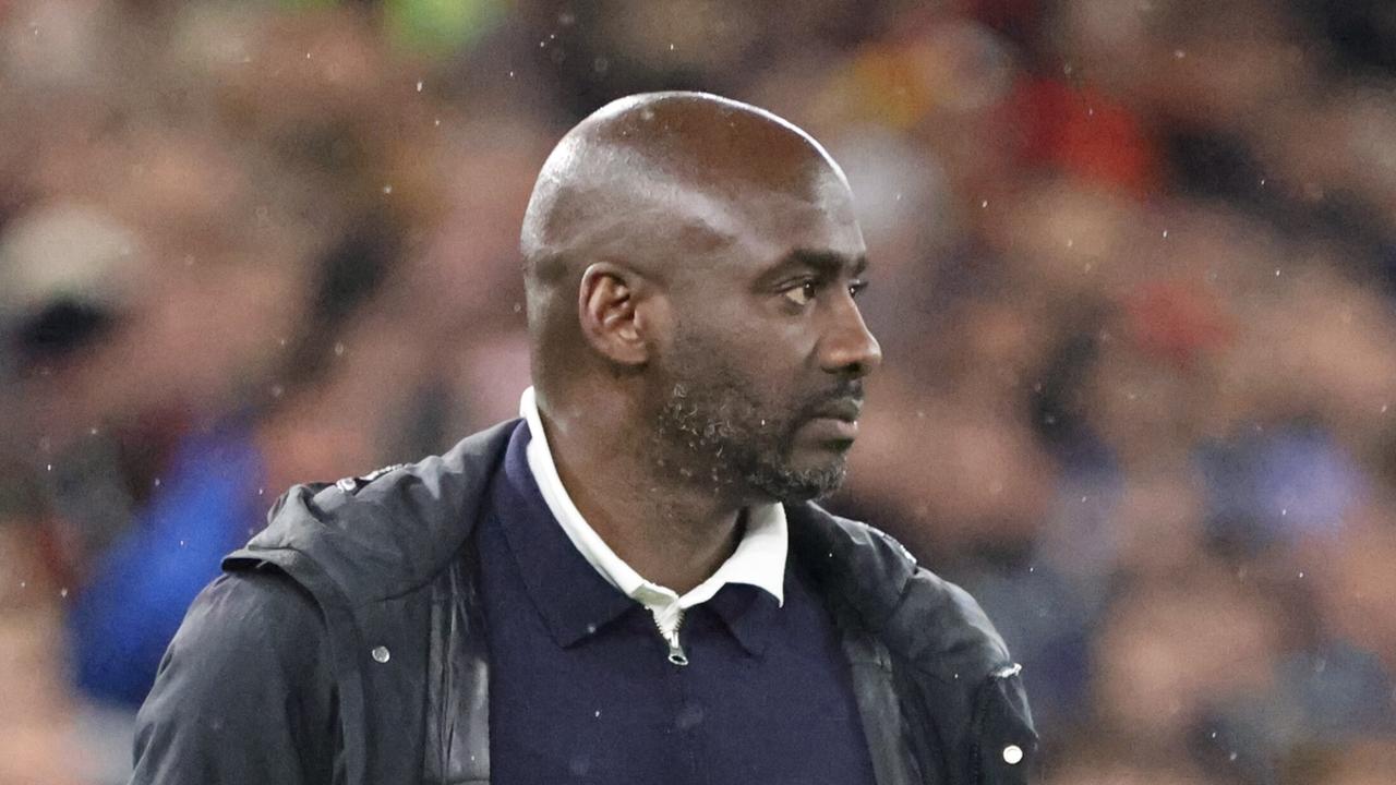 Otto Addo in Pullover und Jacke im Fußballstadion.