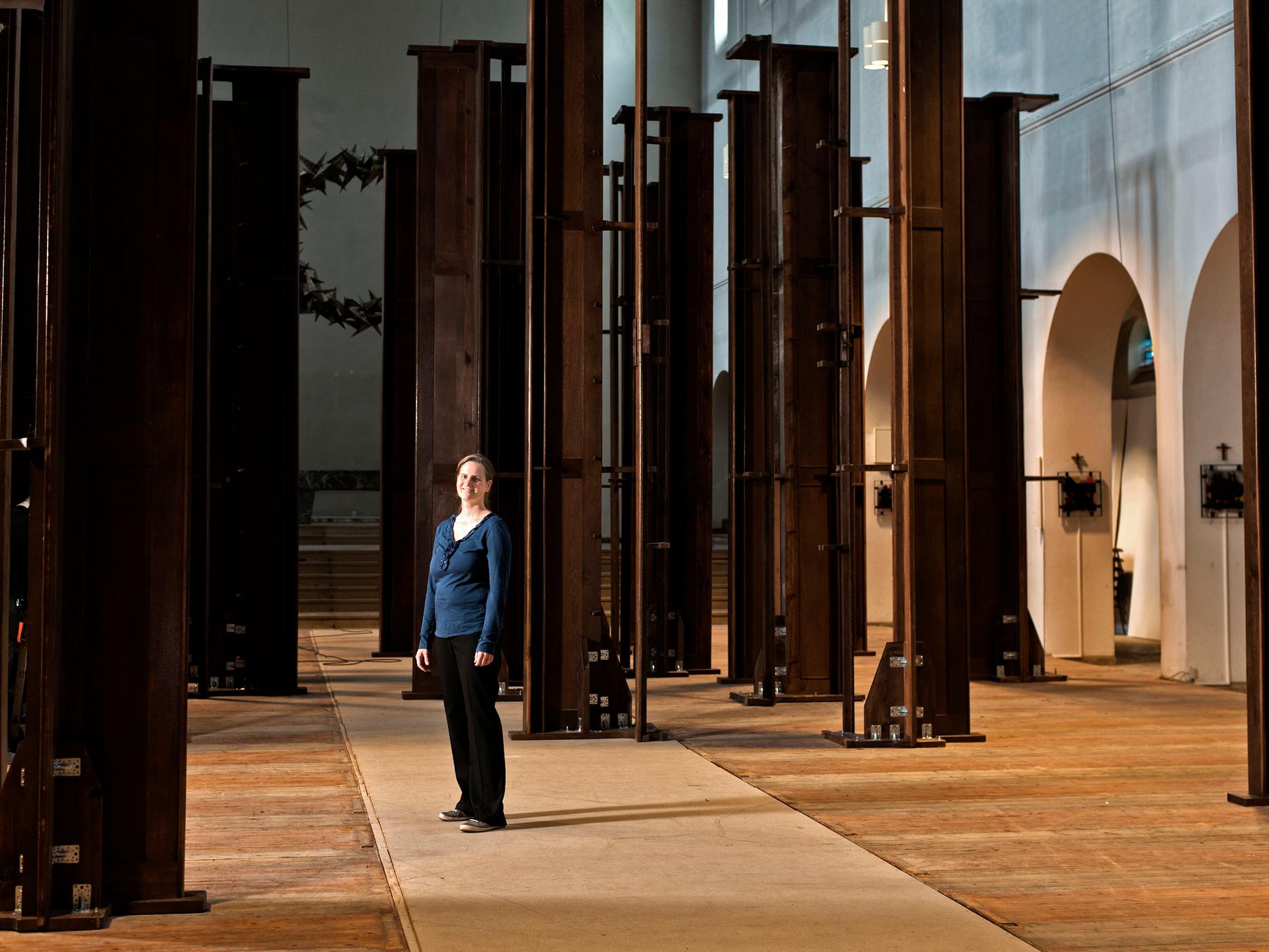 In einer Kirche stehen braune Kirchenbänke senkrecht, in der Mitte steht die Künstlerin Dorothee Bielfeld.