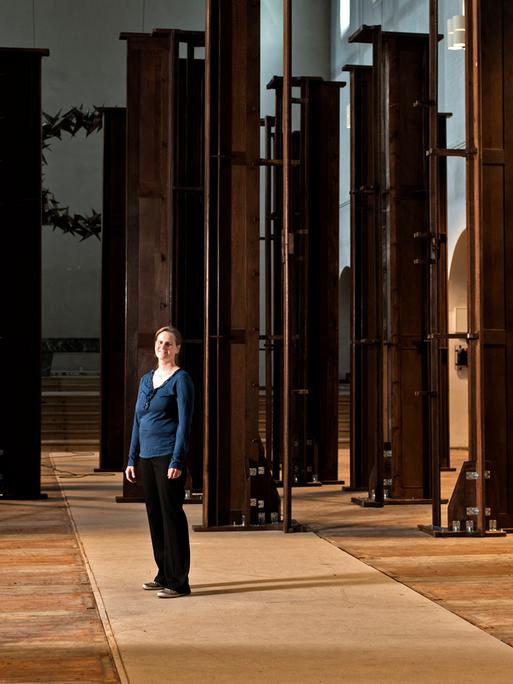 In einer Kirche stehen braune Kirchenbänke senkrecht, in der Mitte steht die Künstlerin Dorothee Bielfeld.