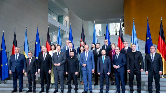 Viele Menschen in Anzügen stehen vor einer Reihe von Fahnen.