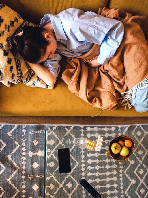 Eine junge Frau liegt auf dem Sofa mit einer Decke