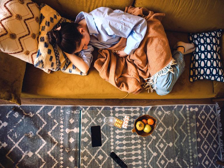 Eine junge Frau liegt auf dem Sofa mit einer Decke