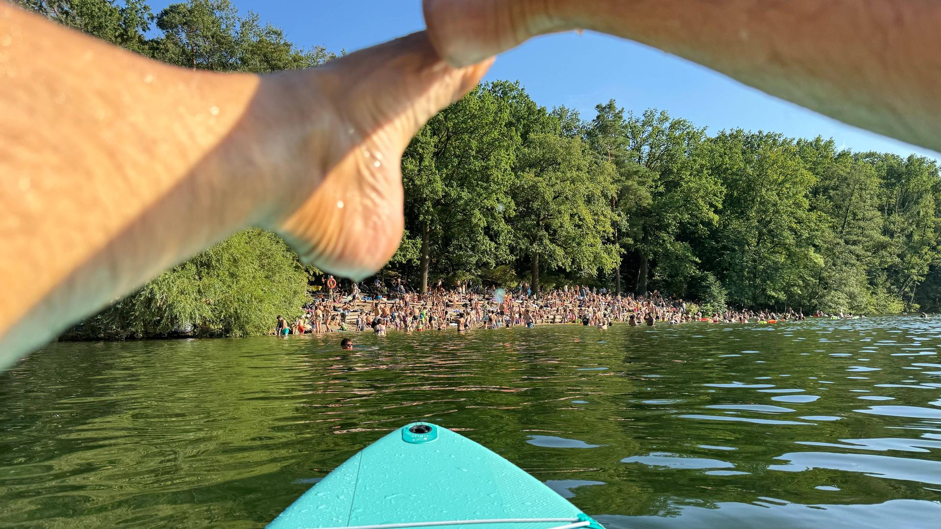 Menschen am Ufer des Sees Krumme Lanke in Berlin aus der Perspektive einer Person auf dem Wasser auf einem Standup-Board.