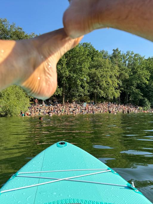 Menschen am Ufer des Sees Krumme Lanke in Berlin aus der Perspektive einer Person auf dem Wasser auf einem Standup-Board.