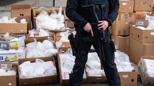 Ein Polizist steht vor Kartons. In den Kartons sind Tüten voller Kokain.