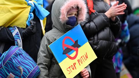 Ein junger Demonstrant hält ein Plakat in den Farben der ukrainischen Flagge, mit der Aufschrift „Stop Putin“ und der Darstellung einer Rakete, die mit einem roten Verbotszeichen versehen ist, in seinen Händen.