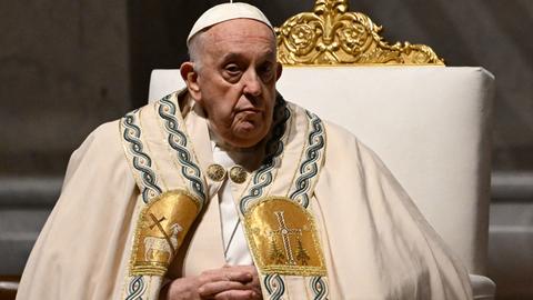 Papst Franziskus in hellem und verziertem Ornat sitzt auf einem gepolsterten Sessel auf dem Altar des Petersdoms