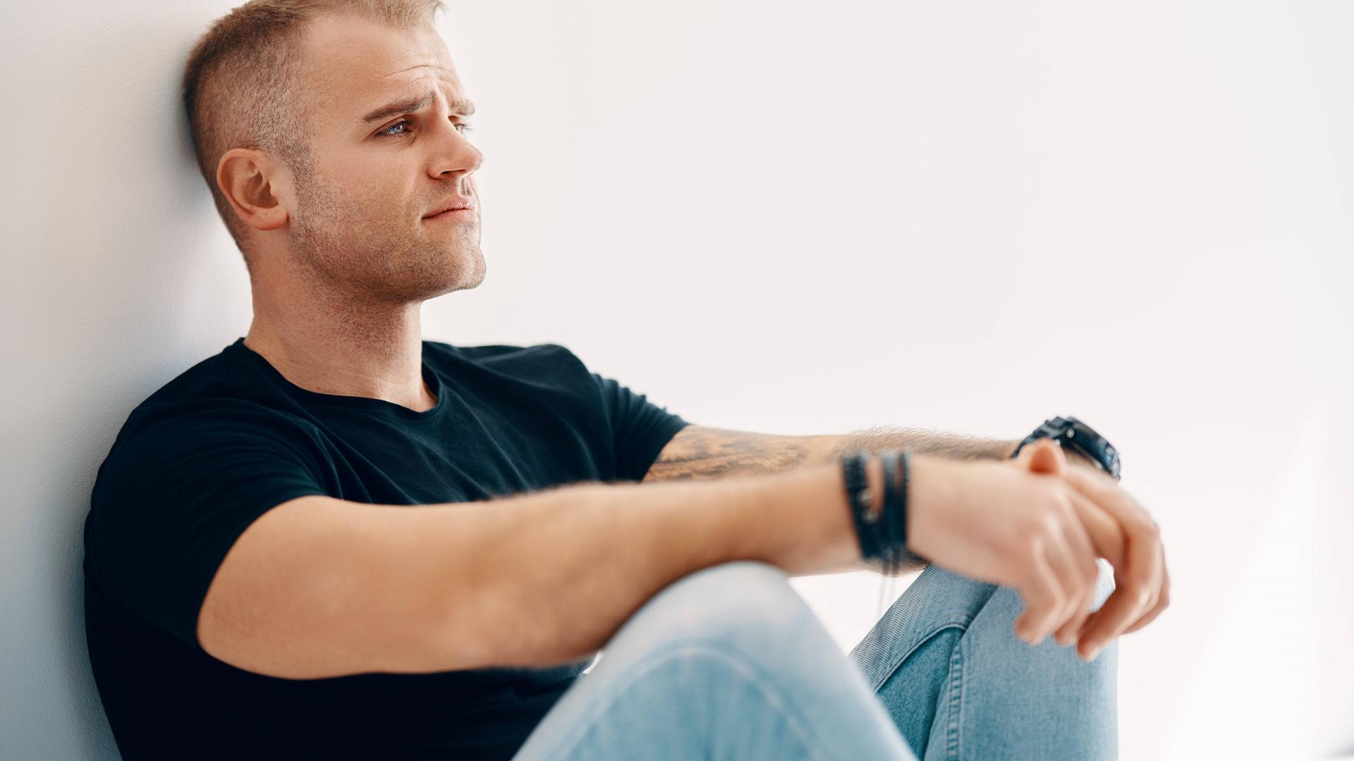 Ein Mann sitzt auf dem Boden und schaut traurig. Ein Mann sitzt auf dem Boden und schaut traurig.