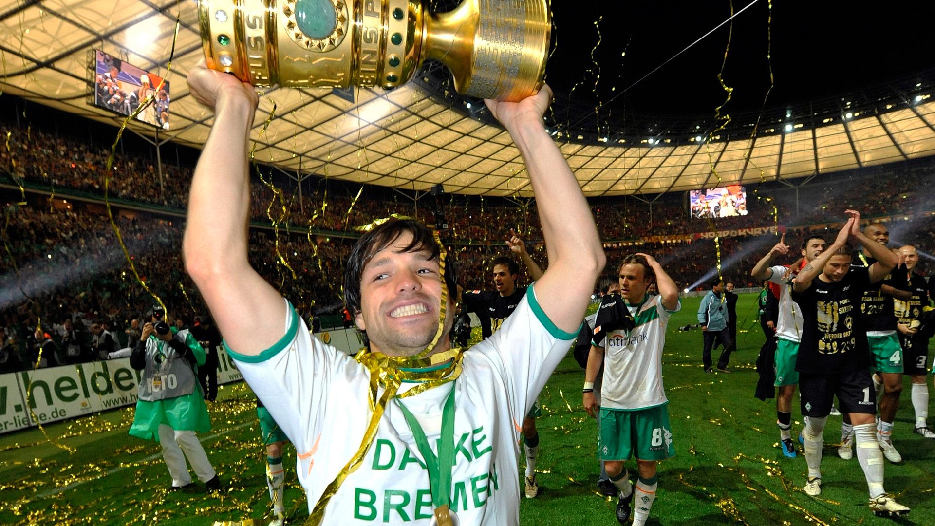 Diego hebt den DFB-Pokal mit beiden Händen über seien Kopf. Er trägt ein Trikot mit der Aufschrift "Danke Bremen" und lacht. 