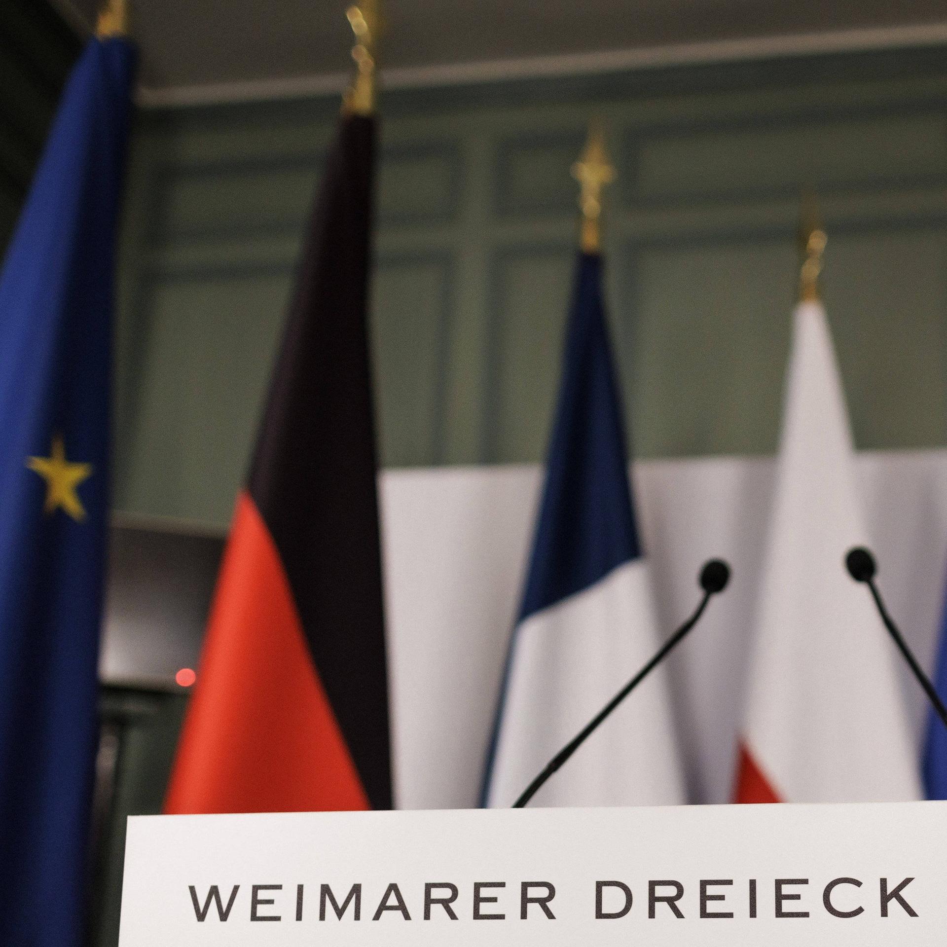 Ein Rednerpult steht vor der Pressekonferenz im Rahmen des Treffen des Weimarer Dreiecks im Schloss de la Celle in La Celle-Saint-Cloud am 12.02.2024 in einem Saal. Dahinter die Länder- und die EU-Fahnen.