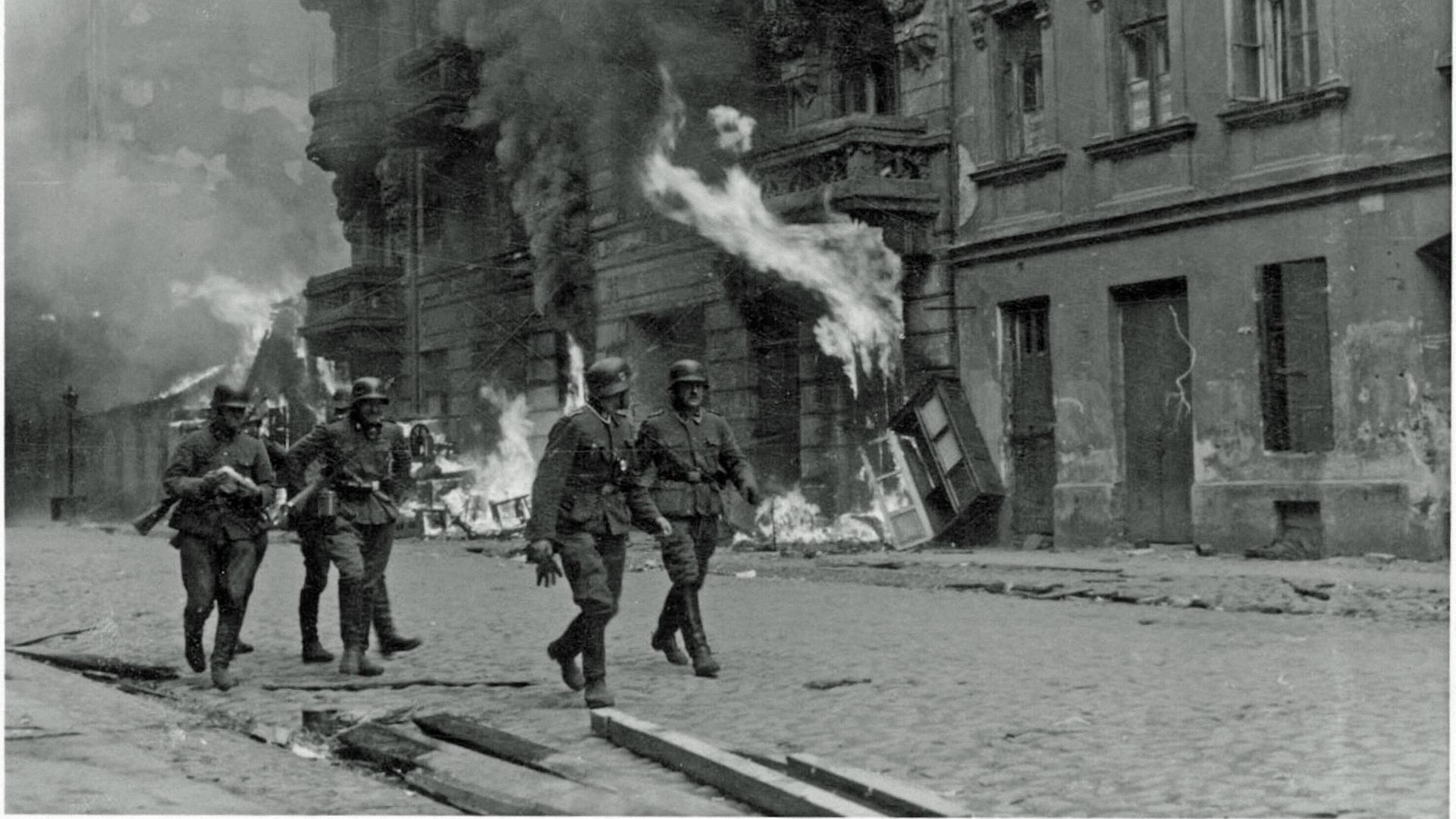 Deutsche SS-Männer gehen im Warschauer Ghetto 1943 an einem brennenden Haus vorbei.