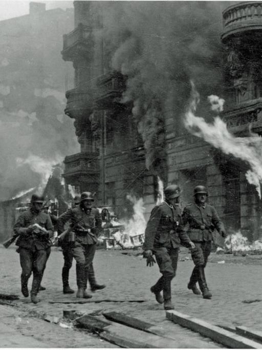 Deutsche SS-Männer gehen im Warschauer Ghetto 1943 an einem brennenden Haus vorbei.
