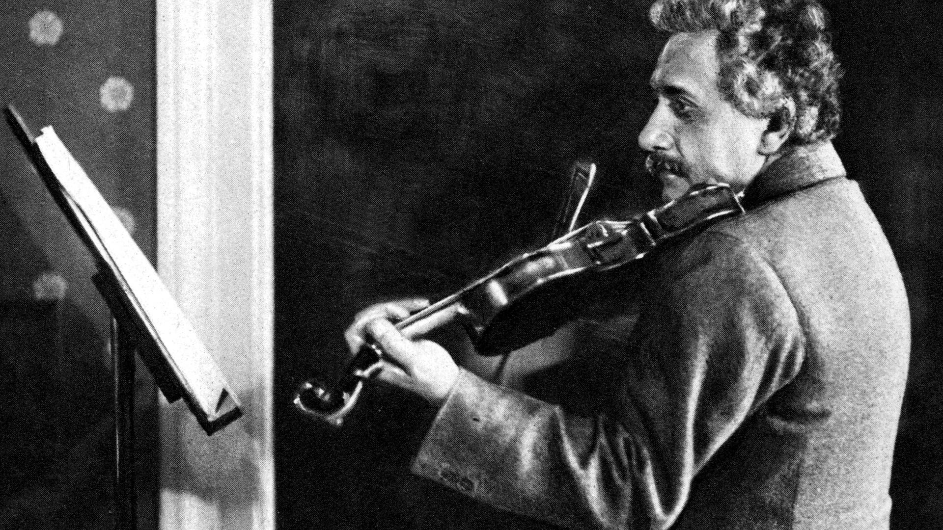 Eine schwarz-weiße Fotografie zeigt den Physiker Albert Einstein vor einem Notenpult Geige spielend.