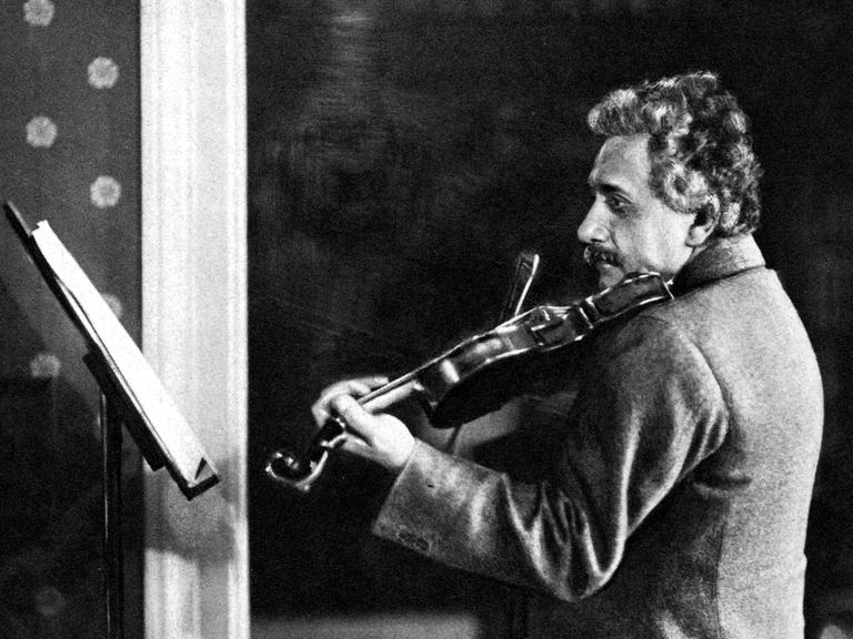 Eine schwarz-weiße Fotografie zeigt den Physiker Albert Einstein vor einem Notenpult Geige spielend.