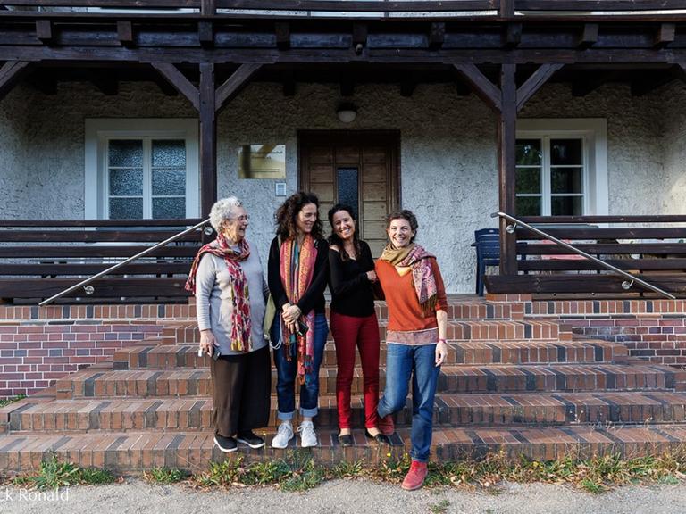 Vier Frauen stehen vor dem Eingang eines historischen, einfachen Hauses.