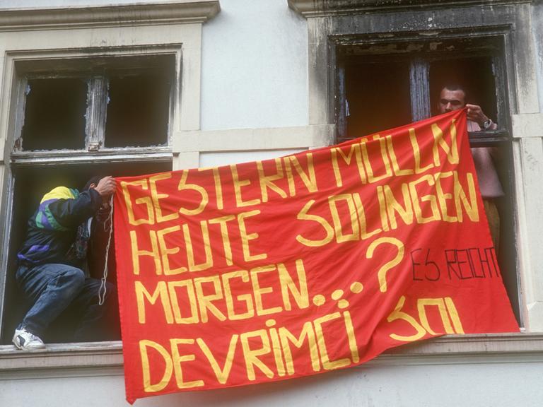 Nach dem rassistischen Brandanschlag auf das Haus der türkischstaemmigen Familie Genc mit 5 Opfern halten zwei Männer eine Fahne durch die verbrannten Fenster, auf der steht: Gestern Mölln, heute Solingen, morgen...?