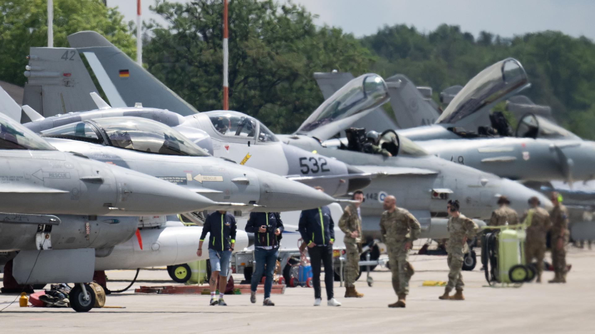 Kampfjets unterschiedlicher Typen stehen auf der US-Airbase Ramstein. Dazwischen sind Soldaten zu sehen. 