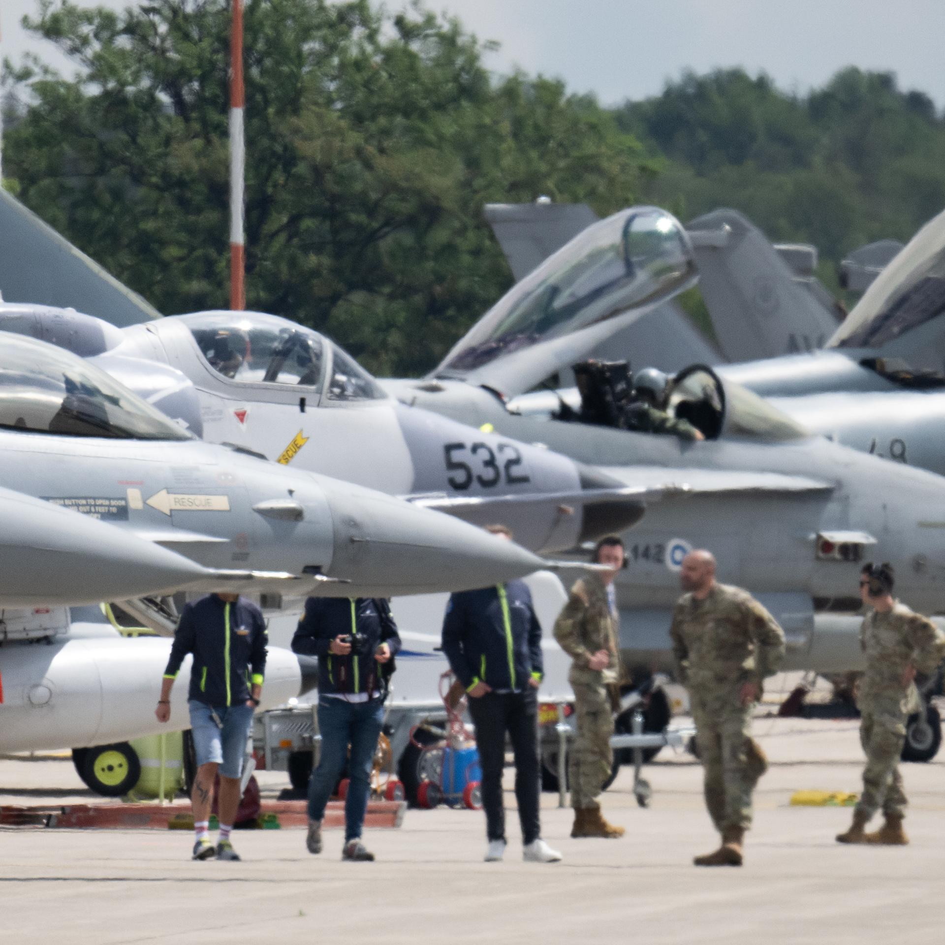 Kampfjets unterschiedlicher Typen stehen auf der US-Airbase Ramstein. Dazwischen sind Soldaten zu sehen. 