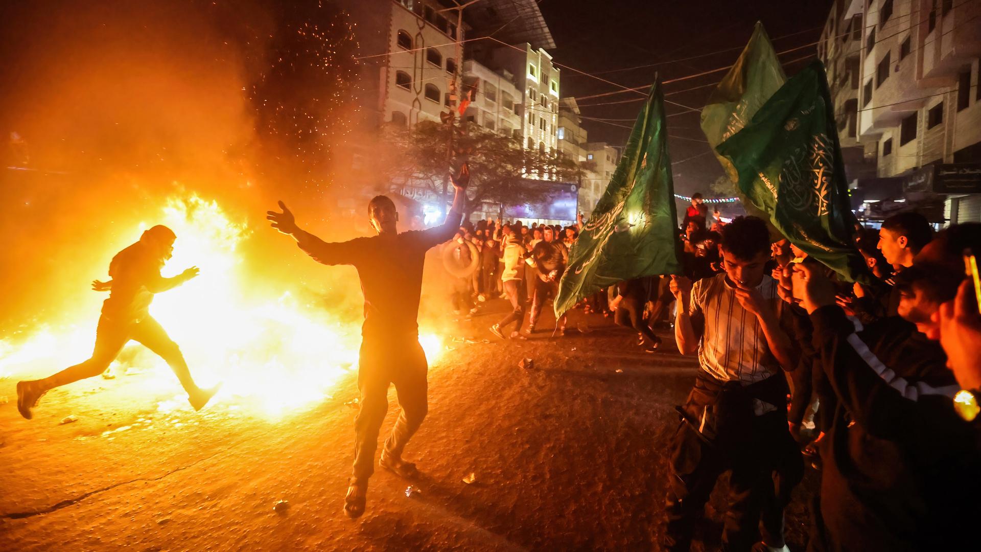 Palästinenser  stehen auf einer Straße in Gaza. Sie tanzen um ein Feuer, in dem sie Flaggen und andere Zeichen Israels verbrennen.